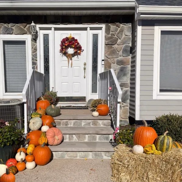 Stone cottage entry with a fall wreath, hay bale, and pumpkins spilling down the steps