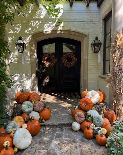 Arched front door along a stone path lined with pumpkins on hay bales